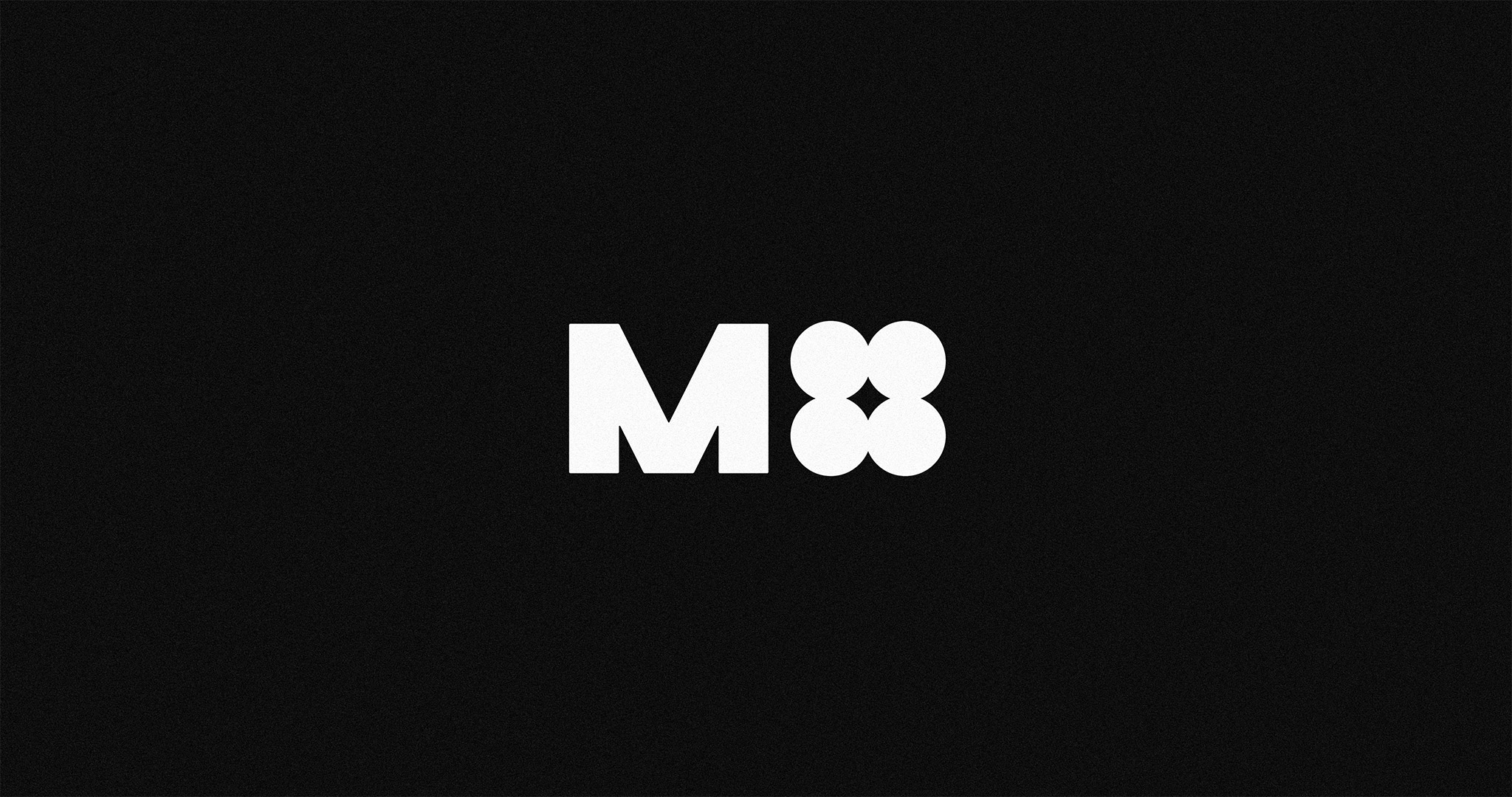 The M4 Music logotype. It features a bold, industrial, uppercase ‘M’, and 4 circles grouped together to represent the number ‘four’. White logotype over black background.