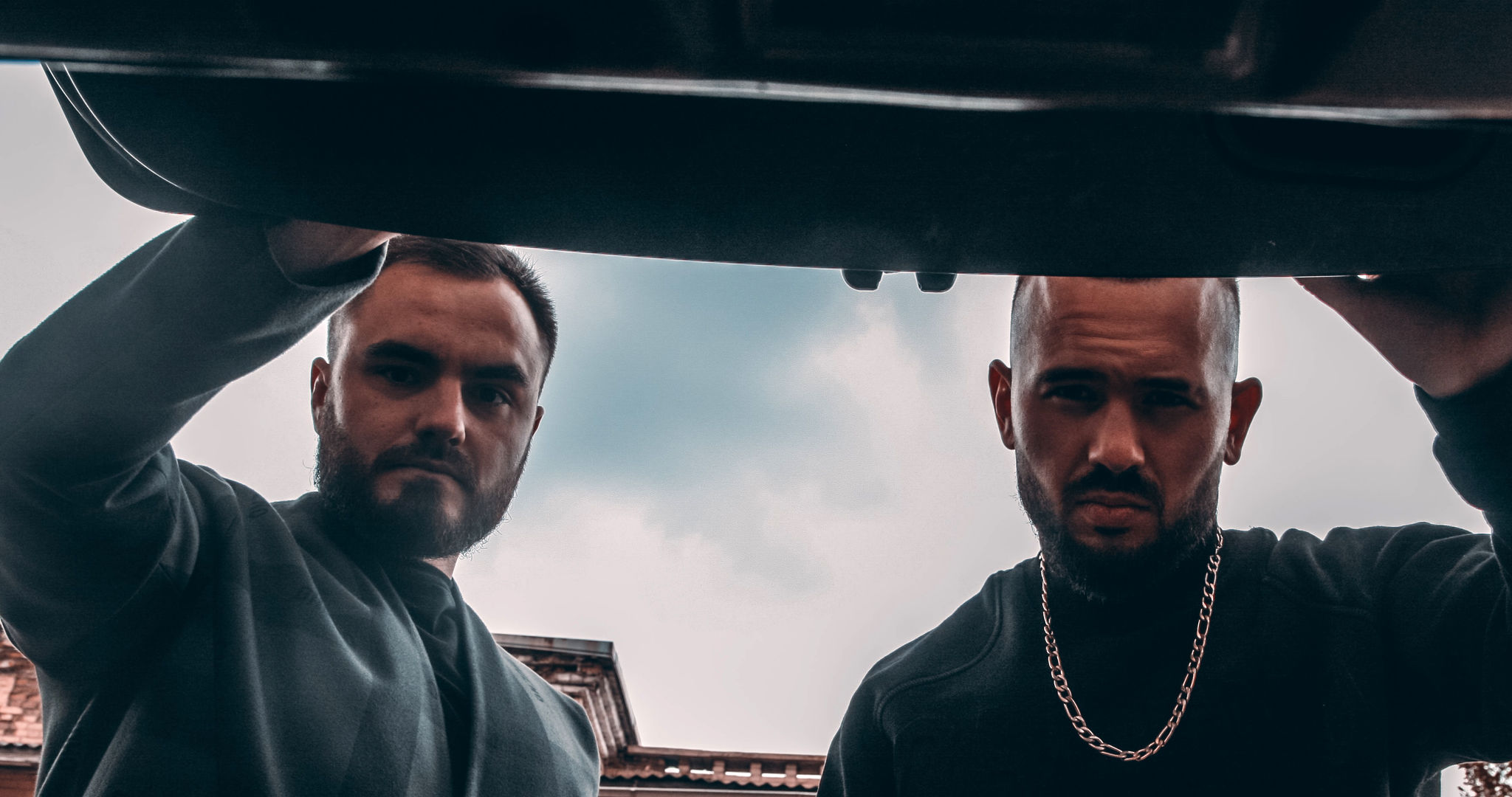 A couple of middle-aged, male kidnappers looking into a car’s trunk.